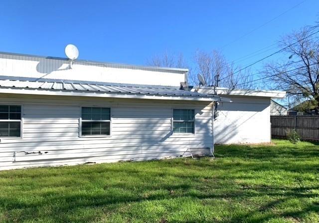 view of side of home with fence, a yard, and metal roof