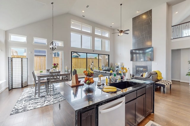 kitchen featuring dishwasher, a sink, high vaulted ceiling, ceiling fan with notable chandelier, and dark stone counters