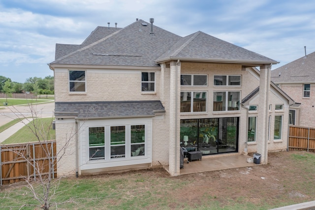 rear view of property with brick siding, a fenced backyard, roof with shingles, and a patio area