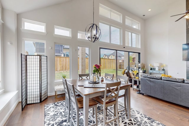 dining area with light wood-style floors, a towering ceiling, ceiling fan with notable chandelier, and a healthy amount of sunlight