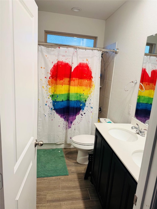 bathroom with double vanity, curtained shower, wood finished floors, a sink, and toilet