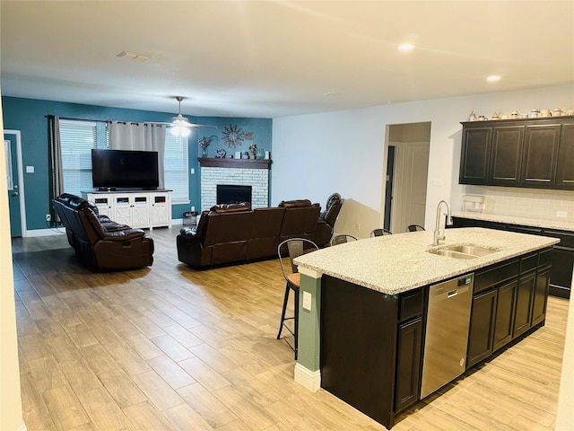 kitchen featuring ceiling fan, a kitchen bar, dishwasher, a sink, and light wood-style floors