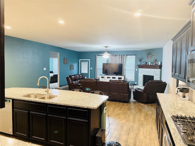 kitchen featuring ceiling fan, a sink, a fireplace, open floor plan, and stainless steel gas stovetop
