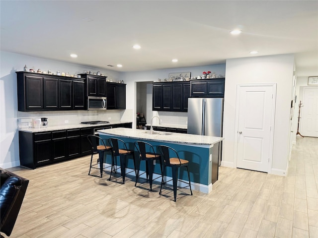 kitchen featuring light wood finished floors, dark cabinetry, a breakfast bar area, stainless steel appliances, and backsplash