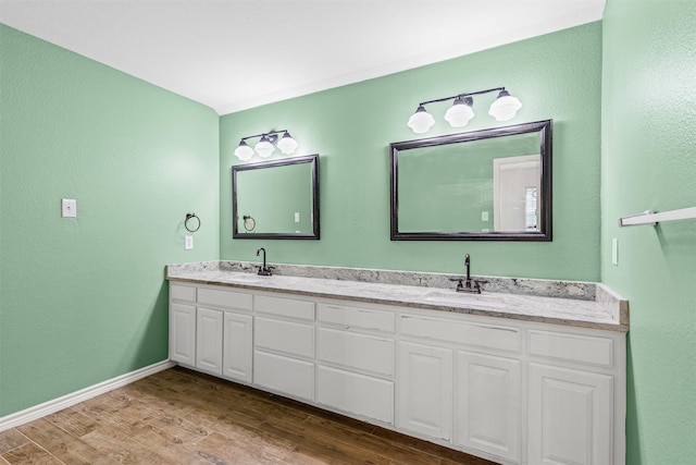 bathroom with double vanity, a textured wall, a sink, and wood finished floors