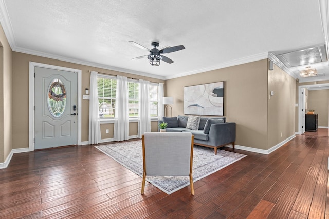 living area featuring baseboards, ornamental molding, a ceiling fan, and attic access