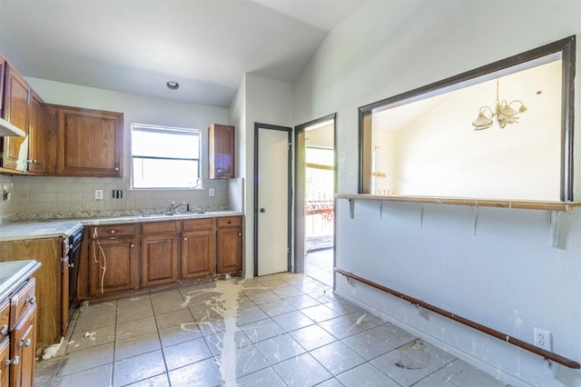 kitchen featuring light countertops, decorative backsplash, brown cabinetry, and a sink