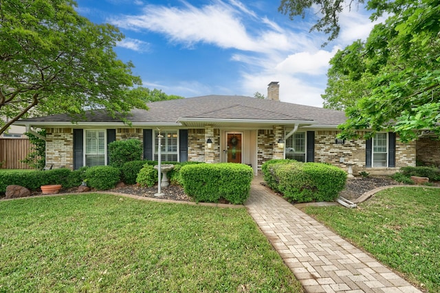 ranch-style house featuring a shingled roof, a chimney, a front lawn, and brick siding