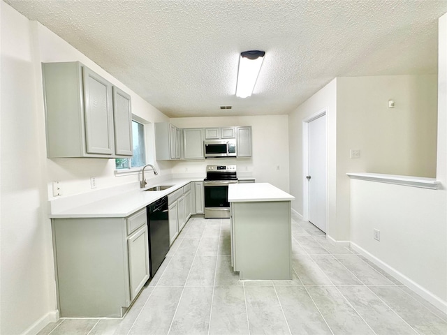 kitchen featuring appliances with stainless steel finishes, a sink, a textured ceiling, a kitchen island, and gray cabinetry