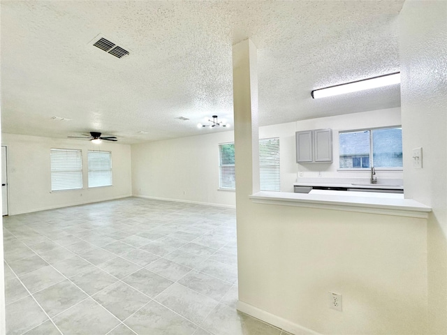 unfurnished living room with visible vents, light tile patterned flooring, ceiling fan, a textured ceiling, and a sink