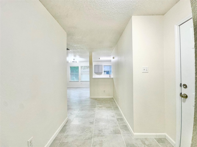 hall featuring a textured ceiling and baseboards