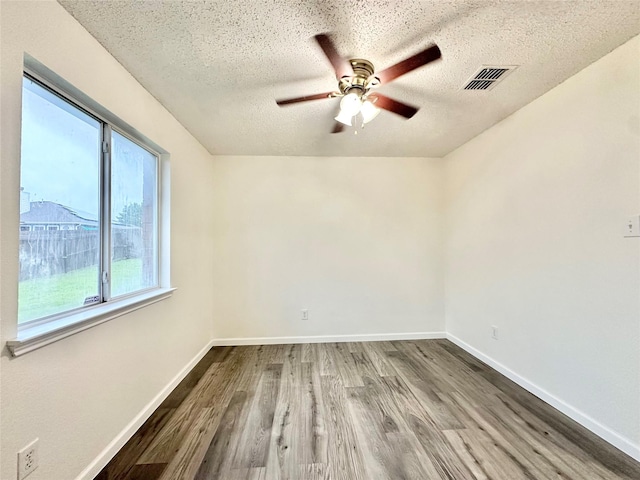 spare room with a textured ceiling, a ceiling fan, baseboards, wood finished floors, and visible vents