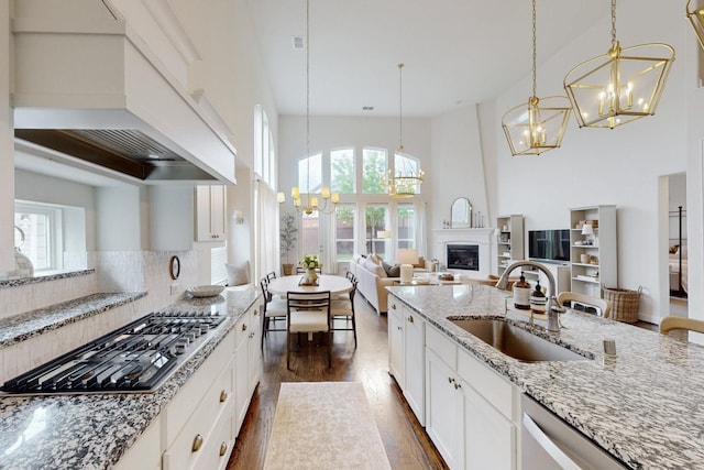 kitchen with dark wood-style floors, a chandelier, custom range hood, a sink, and appliances with stainless steel finishes