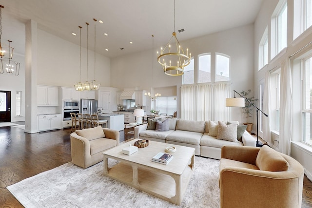living room with a notable chandelier, dark wood-style floors, visible vents, and a towering ceiling