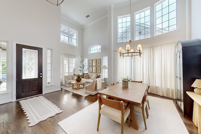 dining area featuring crown molding, a high ceiling, a chandelier, wood finished floors, and visible vents