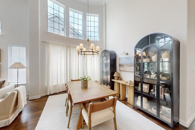 dining space with a towering ceiling, a notable chandelier, baseboards, dark wood-type flooring, and ornamental molding