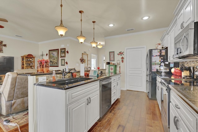 kitchen with crown molding, a sink, stainless steel appliances, white cabinetry, and wood finished floors