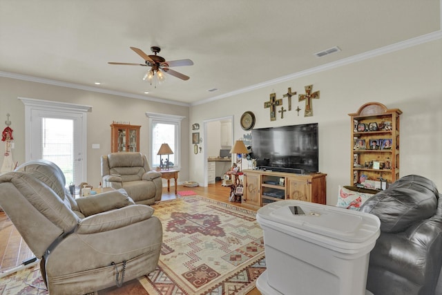 living area featuring crown molding, plenty of natural light, a ceiling fan, and visible vents