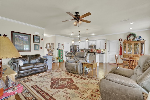 living room featuring ceiling fan, visible vents, wood finished floors, ornamental molding, and recessed lighting