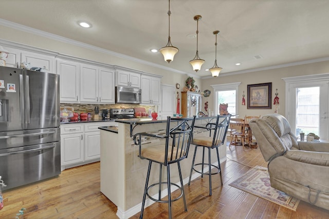 kitchen with dark countertops, open floor plan, a kitchen breakfast bar, light wood-style flooring, and stainless steel appliances