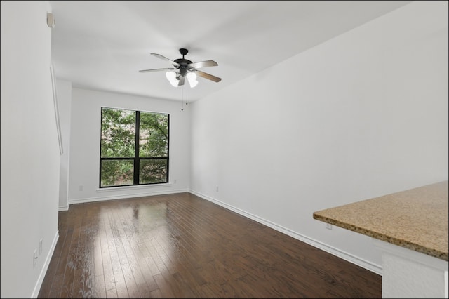 spare room with baseboards, ceiling fan, and dark wood-type flooring