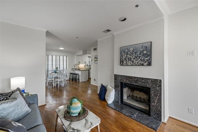 living area with wood finished floors, ornamental molding, visible vents, and a premium fireplace