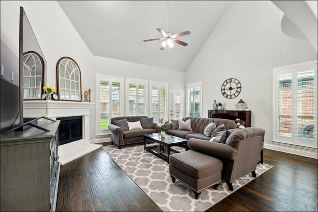 living room featuring ceiling fan, high vaulted ceiling, baseboards, dark wood-style floors, and a glass covered fireplace
