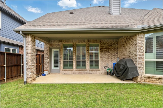 rear view of house featuring fence, roof with shingles, brick siding, a patio area, and a lawn