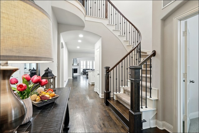 entrance foyer with dark wood-type flooring, arched walkways, baseboards, and stairway