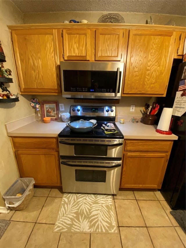 kitchen featuring light countertops, appliances with stainless steel finishes, light tile patterned floors, and brown cabinetry