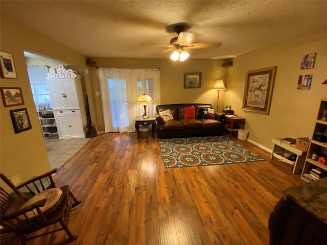 living area featuring baseboards, a ceiling fan, a textured ceiling, and wood finished floors