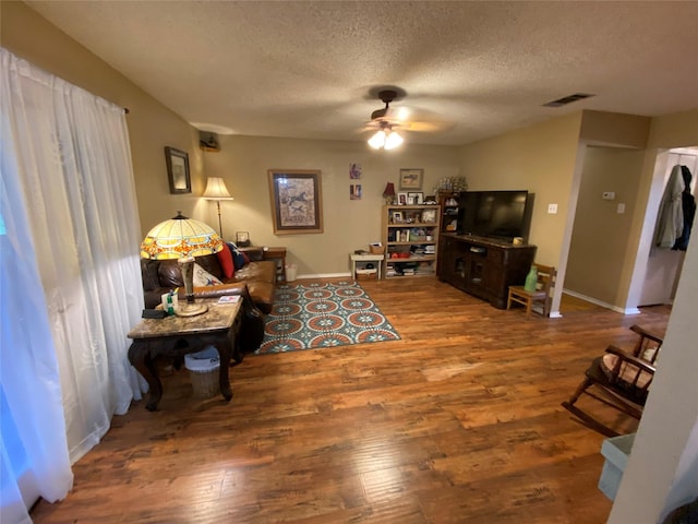 living room with visible vents, wood finished floors, baseboards, a textured ceiling, and a ceiling fan