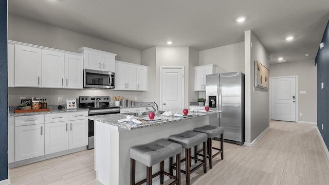 kitchen featuring appliances with stainless steel finishes, a sink, a kitchen island with sink, white cabinetry, and a kitchen bar