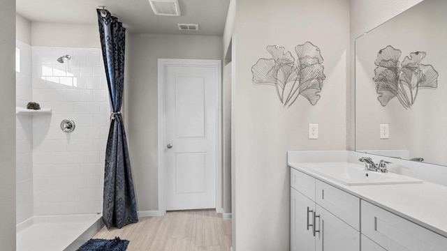 full bath with vanity, baseboards, visible vents, and tiled shower
