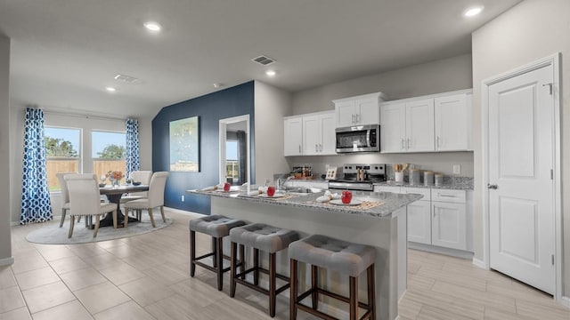 kitchen featuring visible vents, a breakfast bar, a center island with sink, white cabinetry, and stainless steel appliances