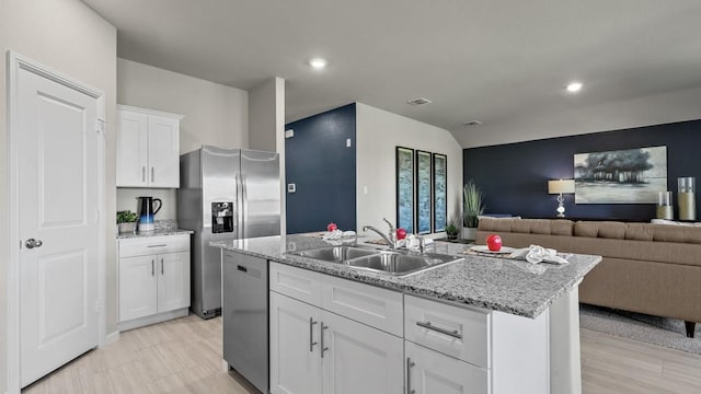 kitchen featuring white cabinets, appliances with stainless steel finishes, a sink, an island with sink, and open floor plan
