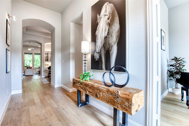 hall featuring arched walkways, baseboards, and light wood-type flooring