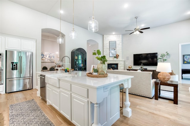 kitchen with a sink, a stone fireplace, ceiling fan, arched walkways, and stainless steel appliances