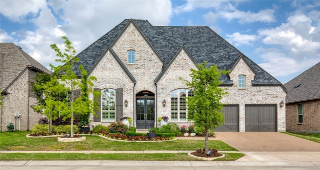 french country inspired facade with brick siding, decorative driveway, and a front yard