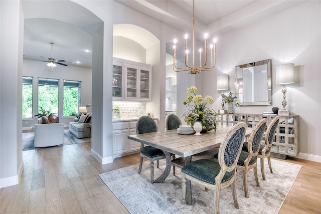 dining area featuring arched walkways, baseboards, light wood finished floors, and ceiling fan with notable chandelier