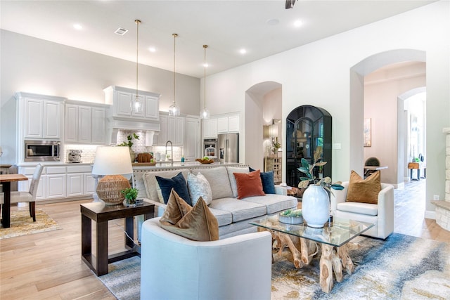 living area featuring visible vents, a high ceiling, recessed lighting, arched walkways, and light wood finished floors