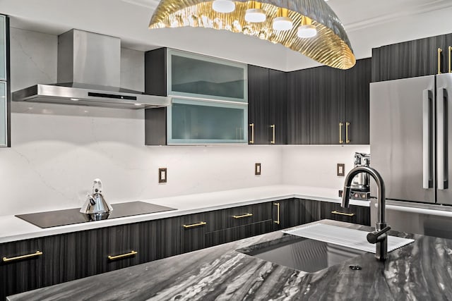 kitchen featuring wall chimney range hood, a sink, freestanding refrigerator, black electric stovetop, and glass insert cabinets