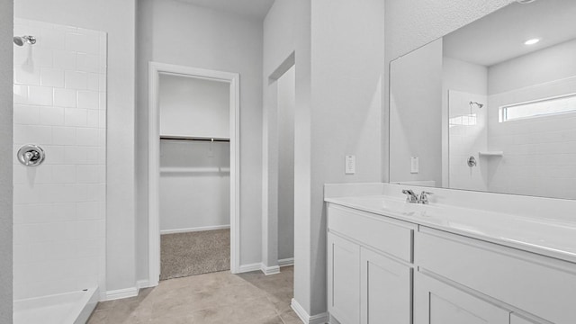 bathroom with a spacious closet, tiled shower, and vanity