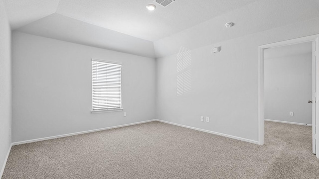 spare room featuring baseboards, carpet, vaulted ceiling, and visible vents