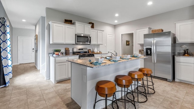 kitchen featuring a center island with sink, light stone counters, white cabinets, a breakfast bar, and stainless steel appliances