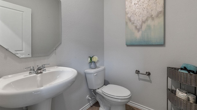 bathroom featuring toilet, baseboards, and a sink