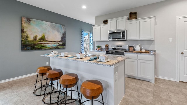 kitchen with baseboards, an island with sink, a kitchen breakfast bar, white cabinets, and stainless steel appliances