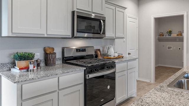 kitchen featuring light stone countertops, baseboards, white cabinetry, a sink, and appliances with stainless steel finishes