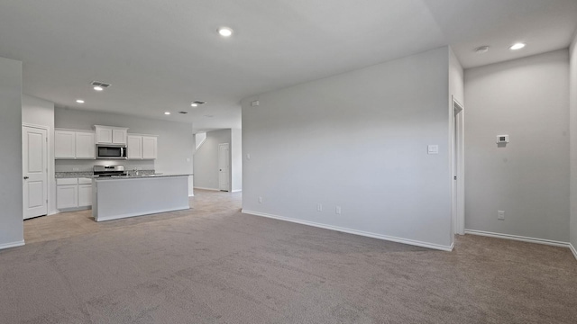 unfurnished living room featuring baseboards, light carpet, and recessed lighting