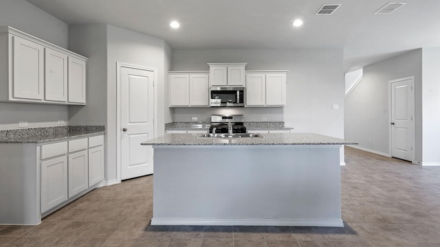 kitchen featuring white cabinets, stainless steel microwave, visible vents, and an island with sink